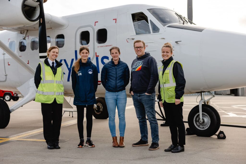 Parents with their teenage daughter standing in front of a Skybus aircraft with 2 female pilots