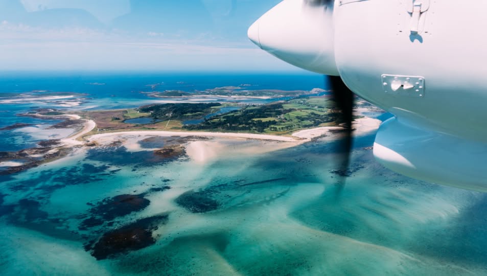 View through an aircraft window showing the Skybus propeller and the turquoise shallows of the Isles of Scilly below.