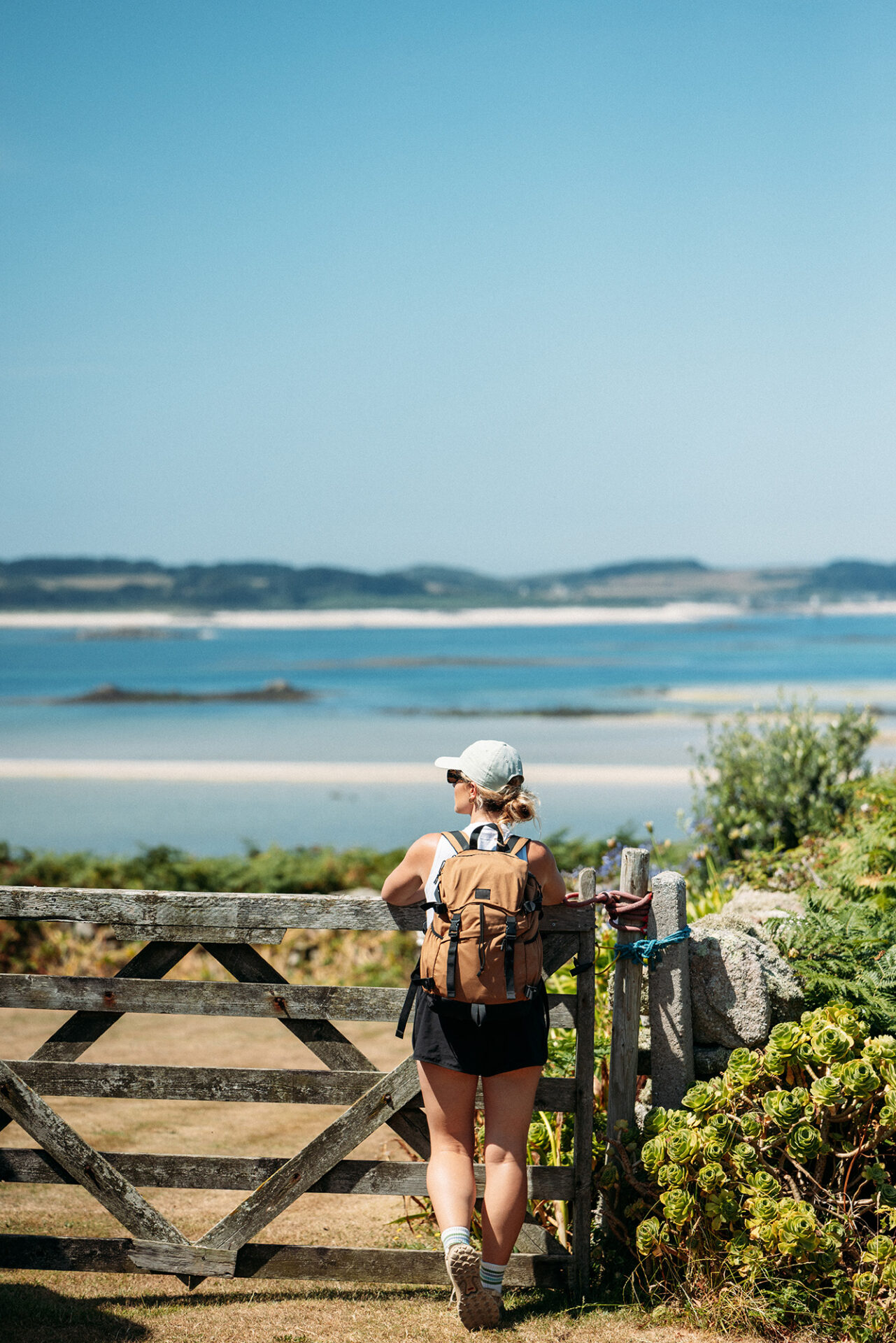 Person in walking gear pausing by a gate on St Martin’s, looking across to neighbouring islands on the horizon.