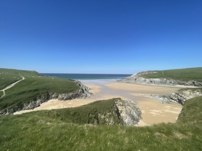 Expansive sandy Porth Joke Beach with clear blue skies and tide out, Cornwall.
