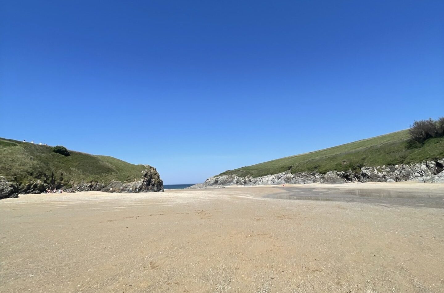 Low-angle view of Porth Joke Beach with wide sands and green cliffs sloping to the sea.