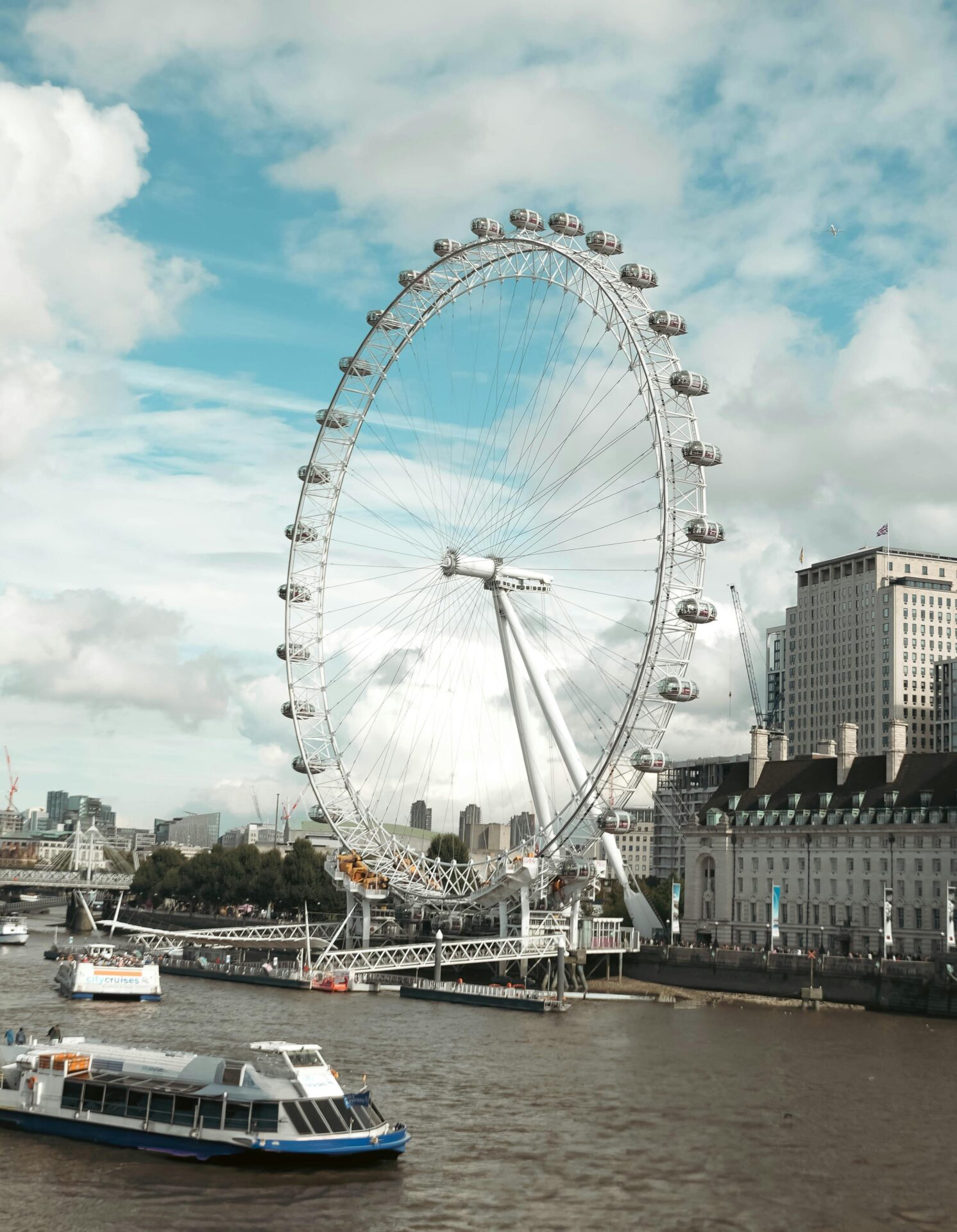 The London Eye towering over the Thames with boats cruising the busy river on a clear day.