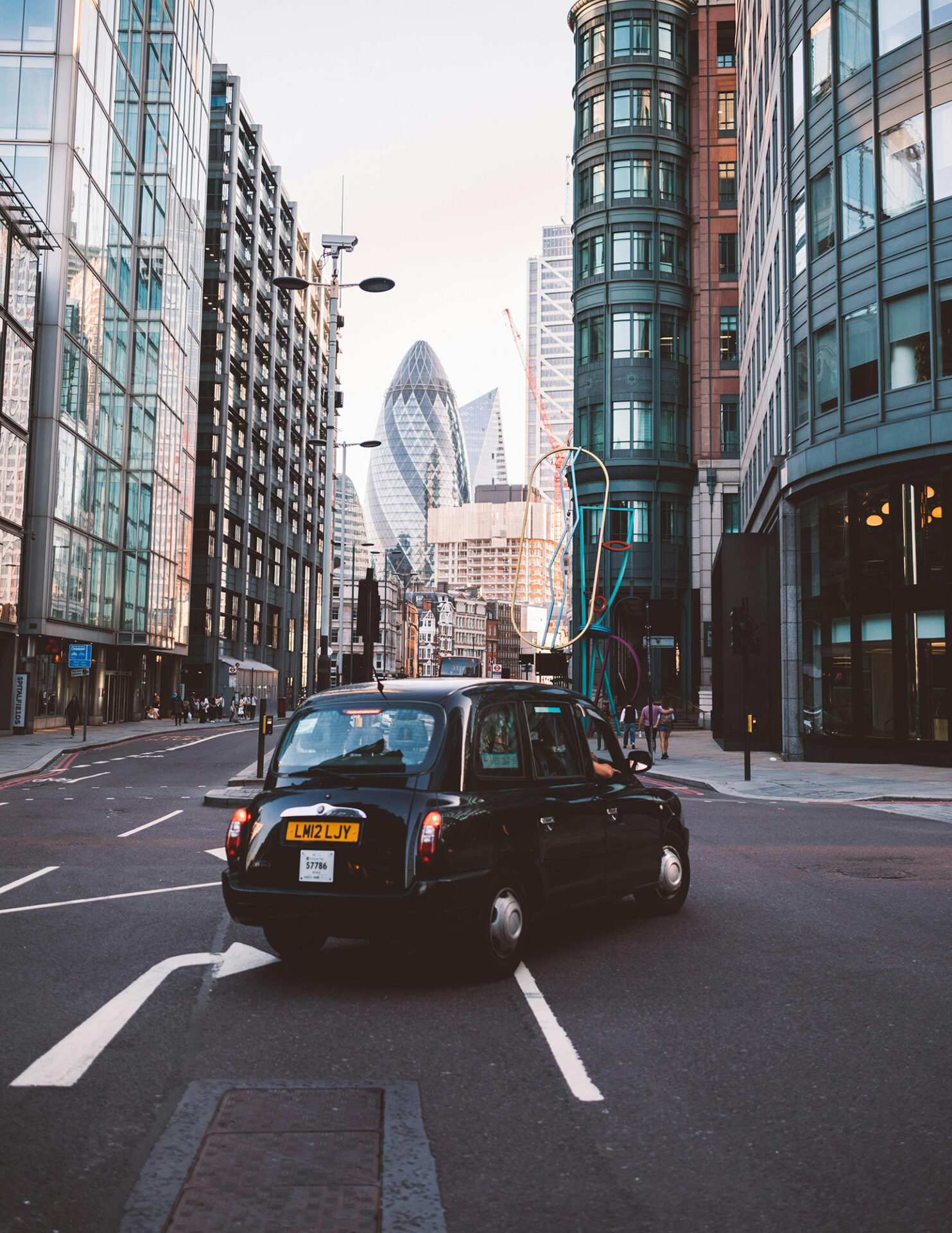 Black cab driving down a modern London street with the Gherkin visible in the background.