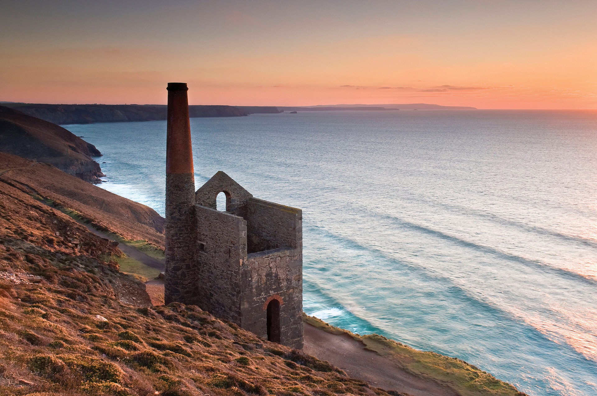 Historic Wheal Coates tin mine silhouetted against a warm sunset with calm seas.