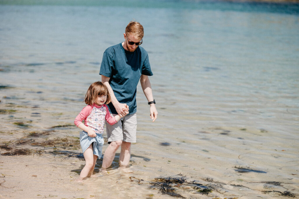 Father and daughter holding hands paddling in the sea on a beach